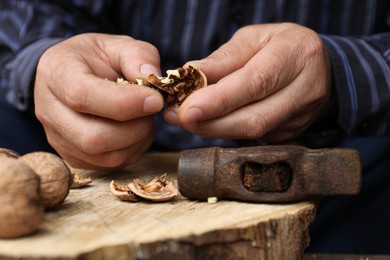 Photo of Man cracking walnuts with hammer at table, closeup
