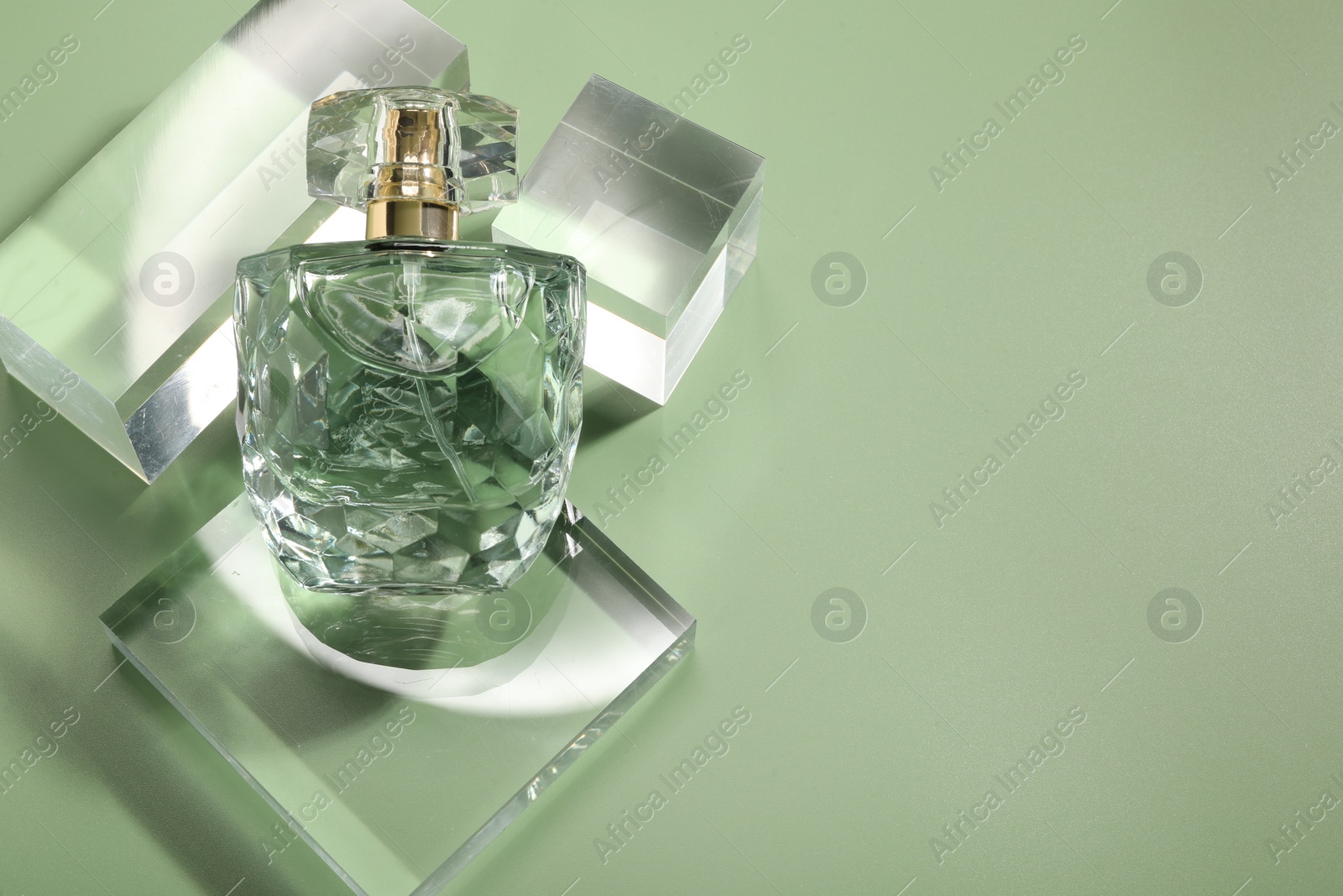 Photo of Stylish presentation of luxury perfume in sunlight on olive background, above view. Space for text