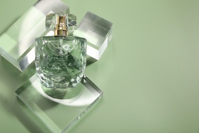 Stylish presentation of luxury perfume in sunlight on olive background, above view. Space for text