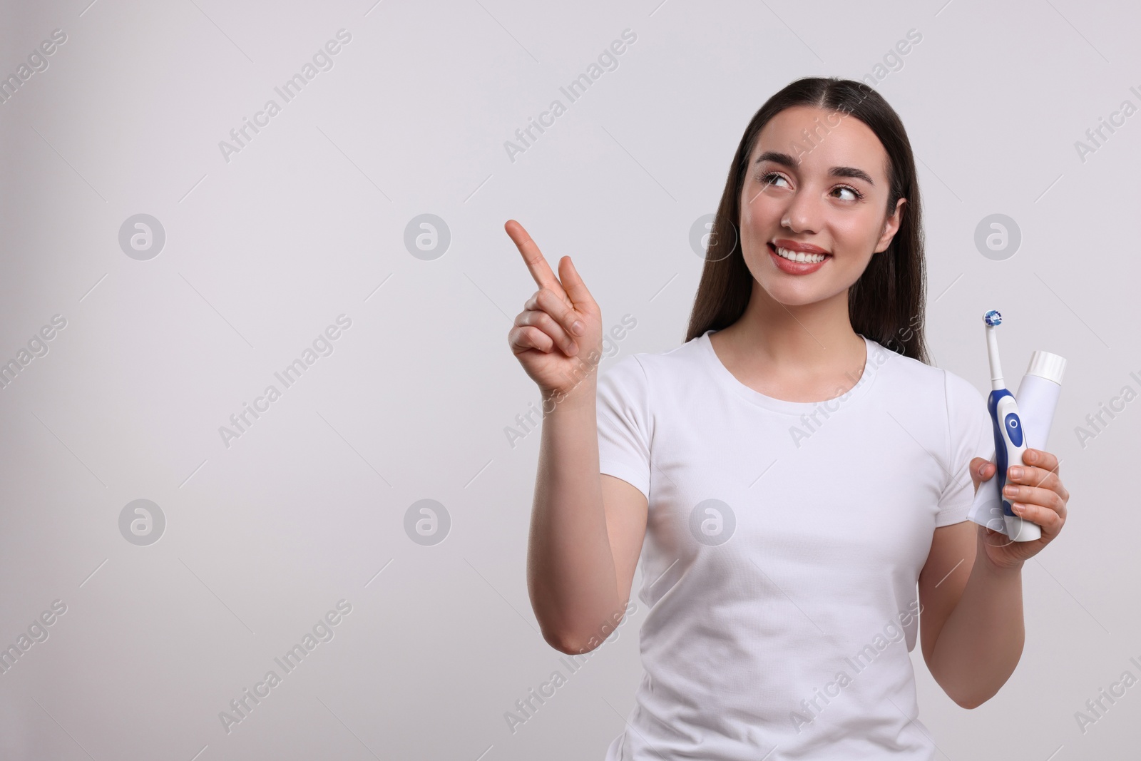 Photo of Happy woman with electric toothbrush and tube of toothpaste pointing on white background, space for text