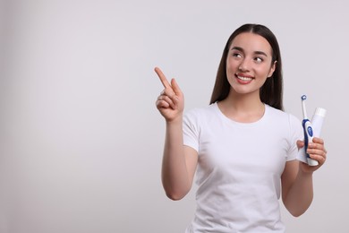 Photo of Happy woman with electric toothbrush and tube of toothpaste pointing on white background, space for text