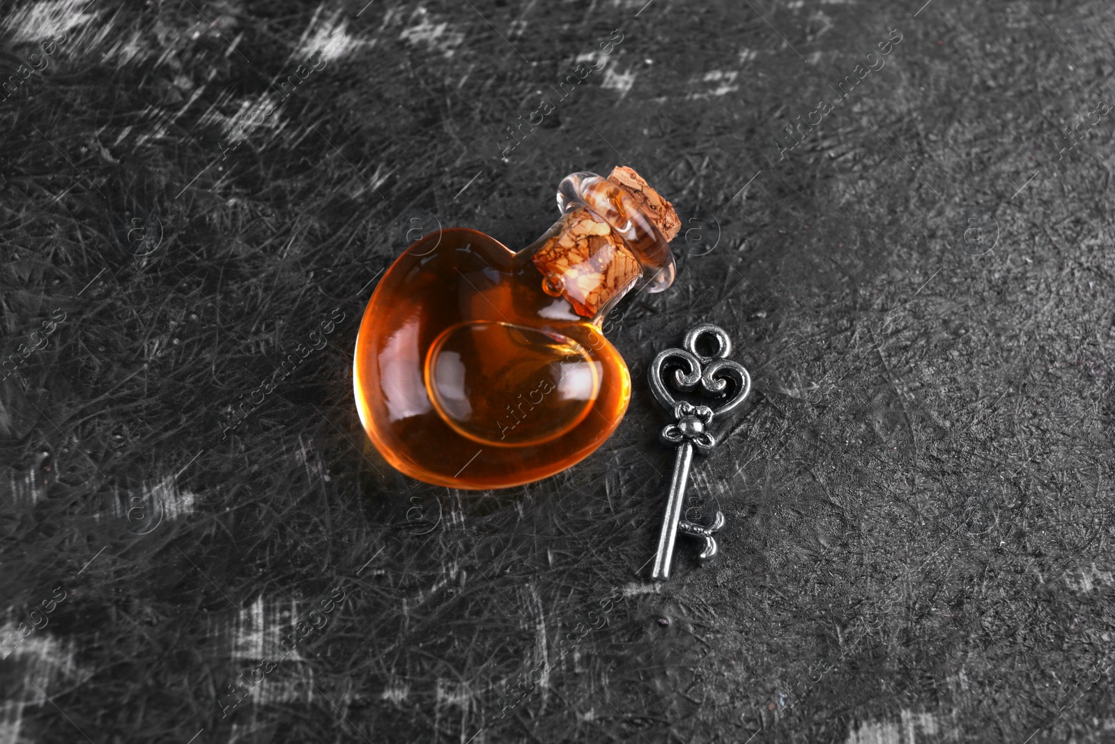 Photo of Heart shaped bottle of love potion with small key on black textured table, flat lay