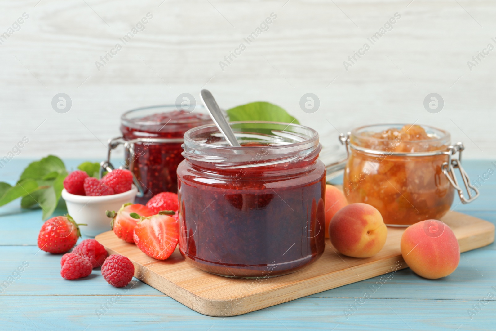 Photo of Jars with different jams and fresh fruits on light blue wooden table