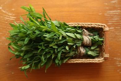 Photo of Bunchesbeautiful green mint in wicker basket on brown wooden table, top view