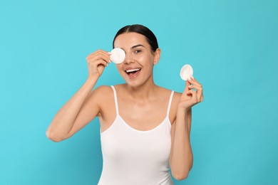 Young woman using cotton pads with micellar water on light blue background