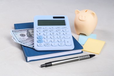 Photo of Calculator, dollar banknotes, piggy bank, notebook, sticky notes and pen on light gray table. Retirement concept