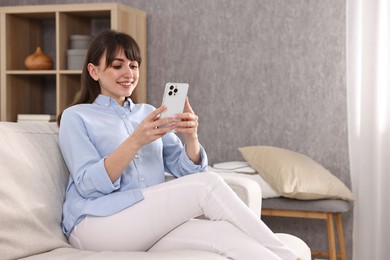 Photo of Beautiful young housewife using smartphone on sofa at home