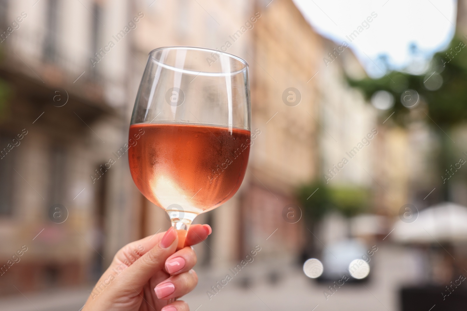 Photo of Woman holding glass of rose wine outdoors, closeup. Space for text