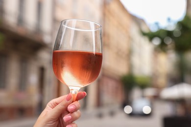 Woman holding glass of rose wine outdoors, closeup. Space for text