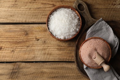 Different natural salt on wooden table, flat lay. Space for text