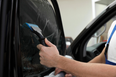 Photo of Worker tinting car window with foil in workshop, closeup