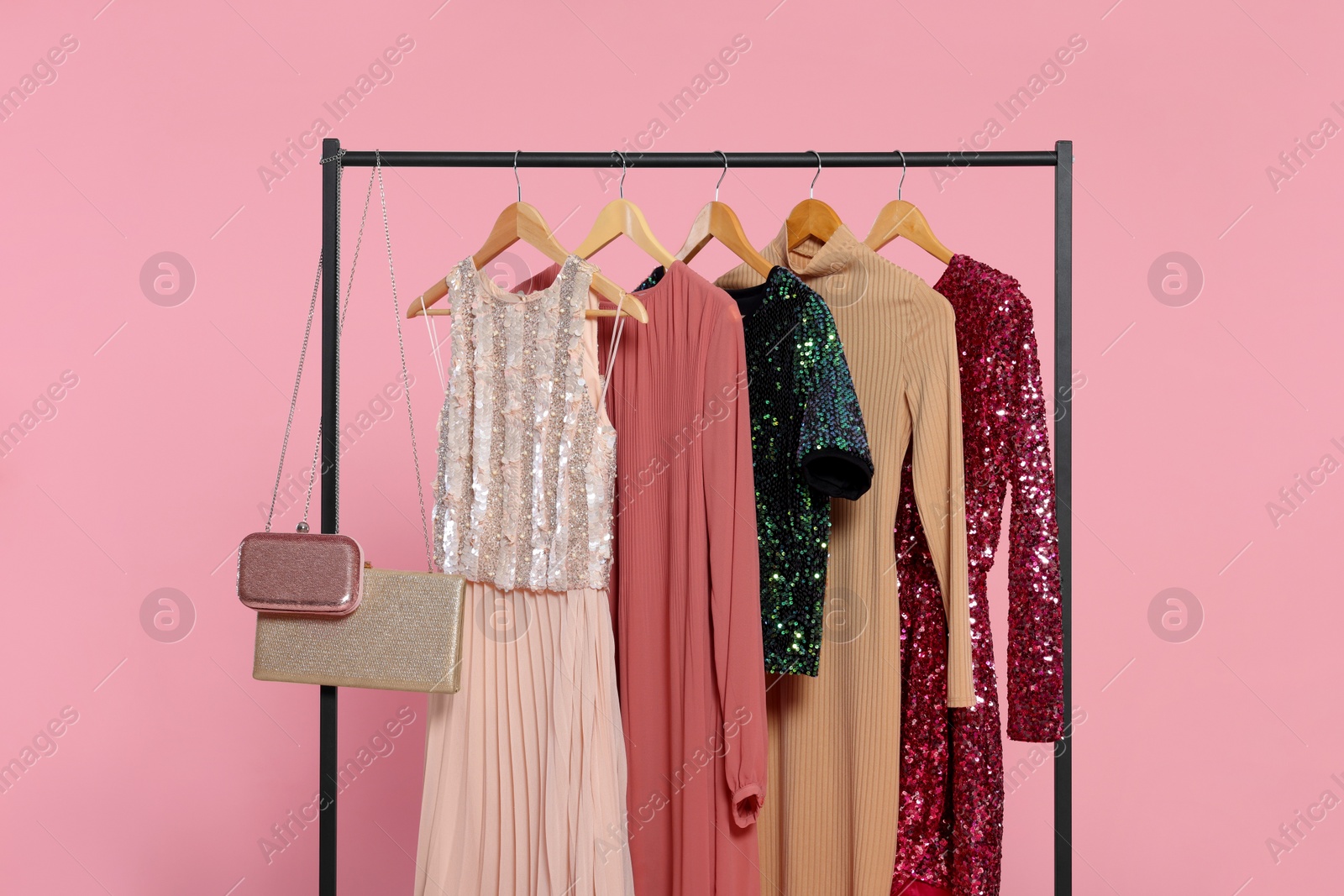 Photo of Rack with stylish women's clothes on wooden hangers and accessories against pink background