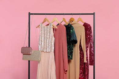 Photo of Rack with stylish women's clothes on wooden hangers and accessories against pink background
