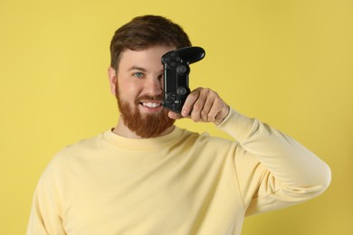 Smiling man with game controller on pale yellow background