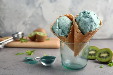 Composition with delicious spirulina ice cream cones in glass on table against grey background. Space for text