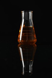 Photo of Glass flask with yellow oil on black background