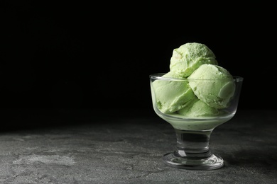 Photo of Delicious pistachio ice cream on grey table against dark background. Space for text