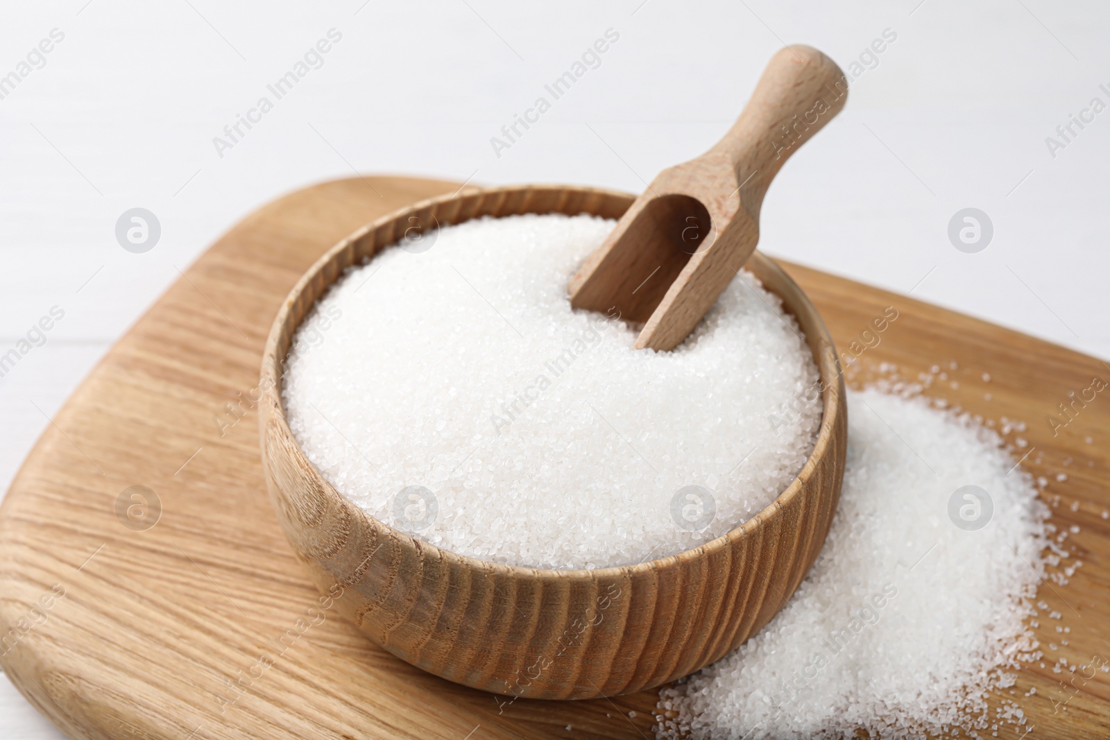 Photo of Wooden bowl with granulated sugar and scoop on white table, closeup