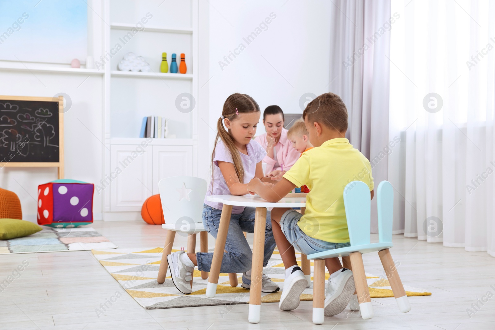 Photo of Cute little children and nursery teacher playing at desk in kindergarten. Playtime activities for motor skills development