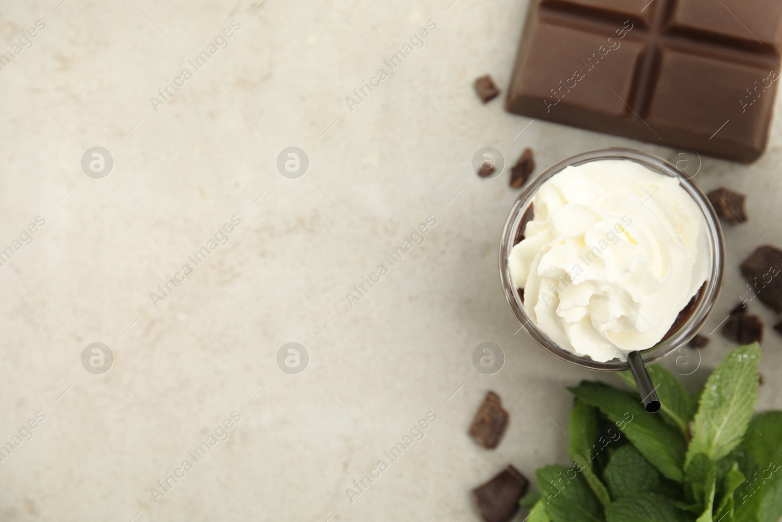 Photo of Glass of delicious hot chocolate with whipped cream, chunks and fresh mint on light table, flat lay. Space for text