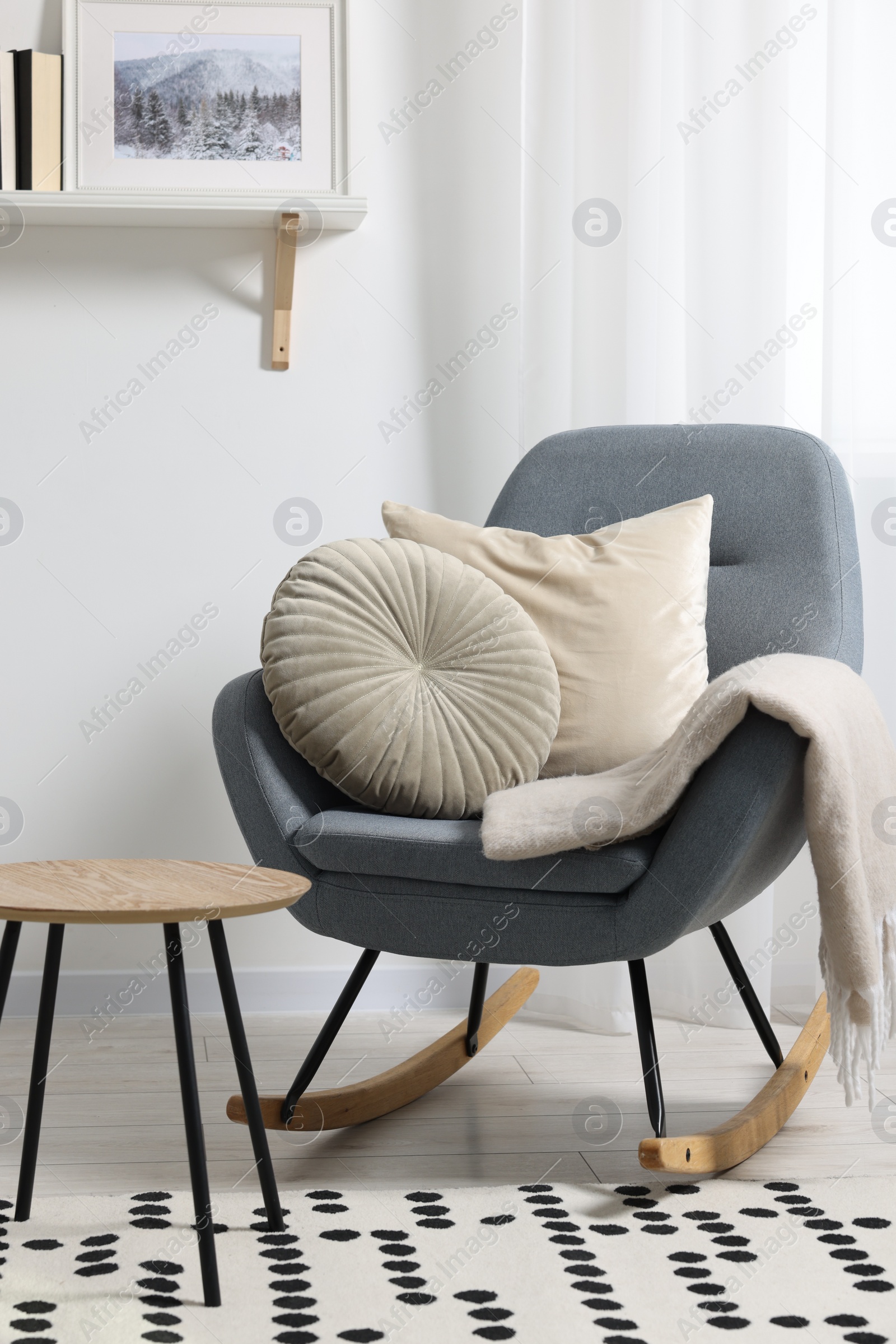 Photo of Soft pillows and blanket on rocking armchair indoors