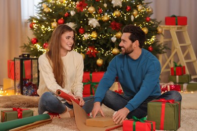 Happy couple decorating Christmas gift with wrapping paper at home