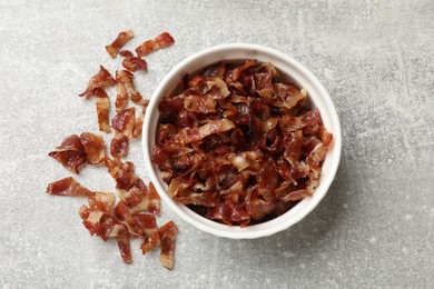 Photo of Pieces of tasty fried bacon in bowl on gray textured table, top view