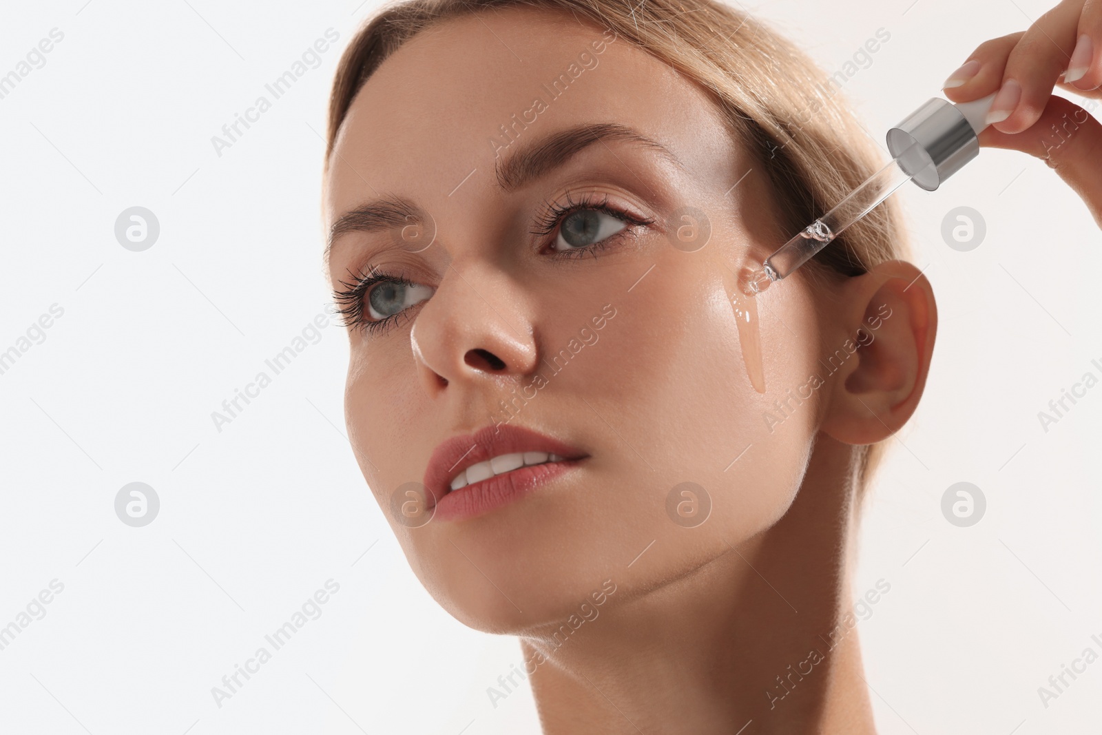 Photo of Beautiful woman applying cosmetic serum onto her face on white background