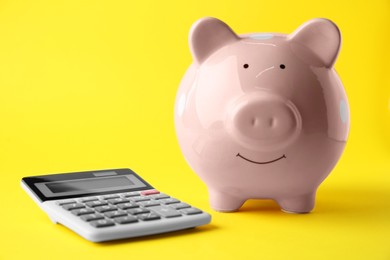 Calculator and pink piggy bank on yellow background, closeup