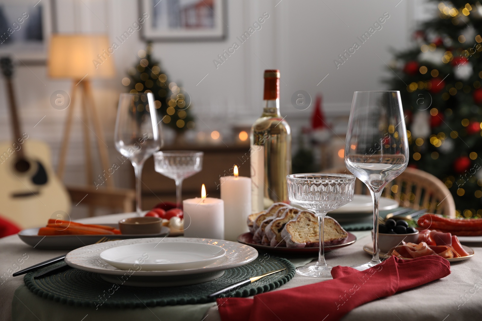 Photo of Christmas table setting with burning candles, appetizers and dishware indoors