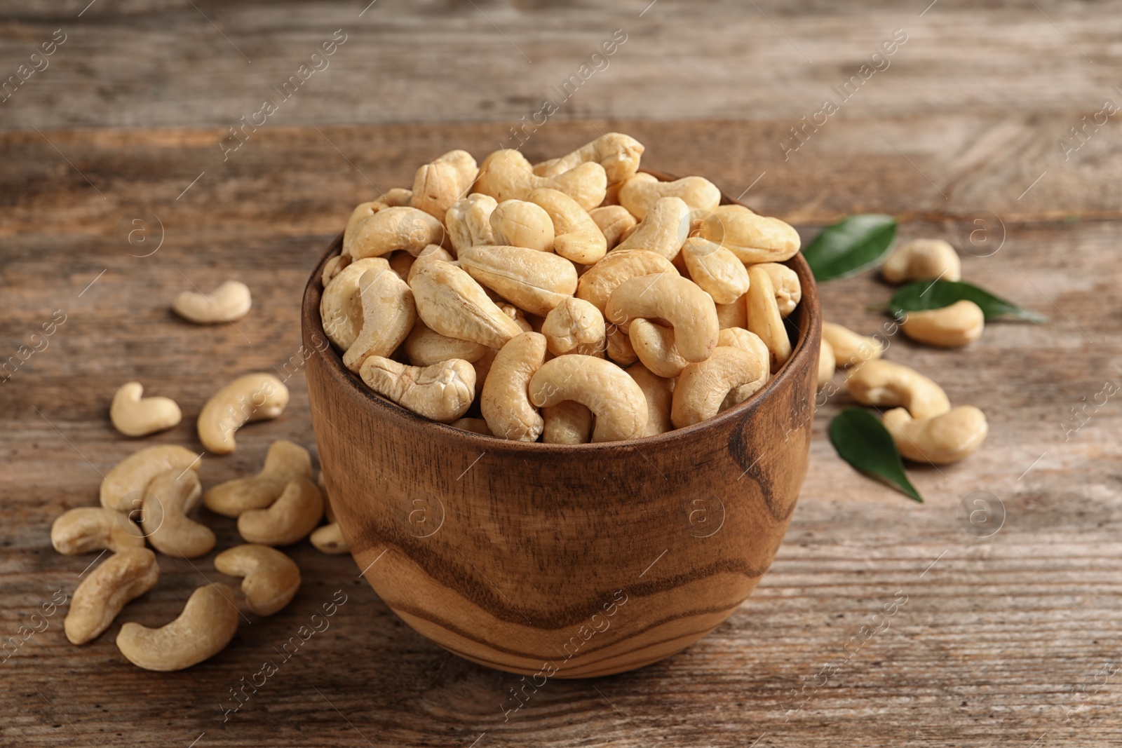 Photo of Tasty cashew nuts in bowl on wooden table