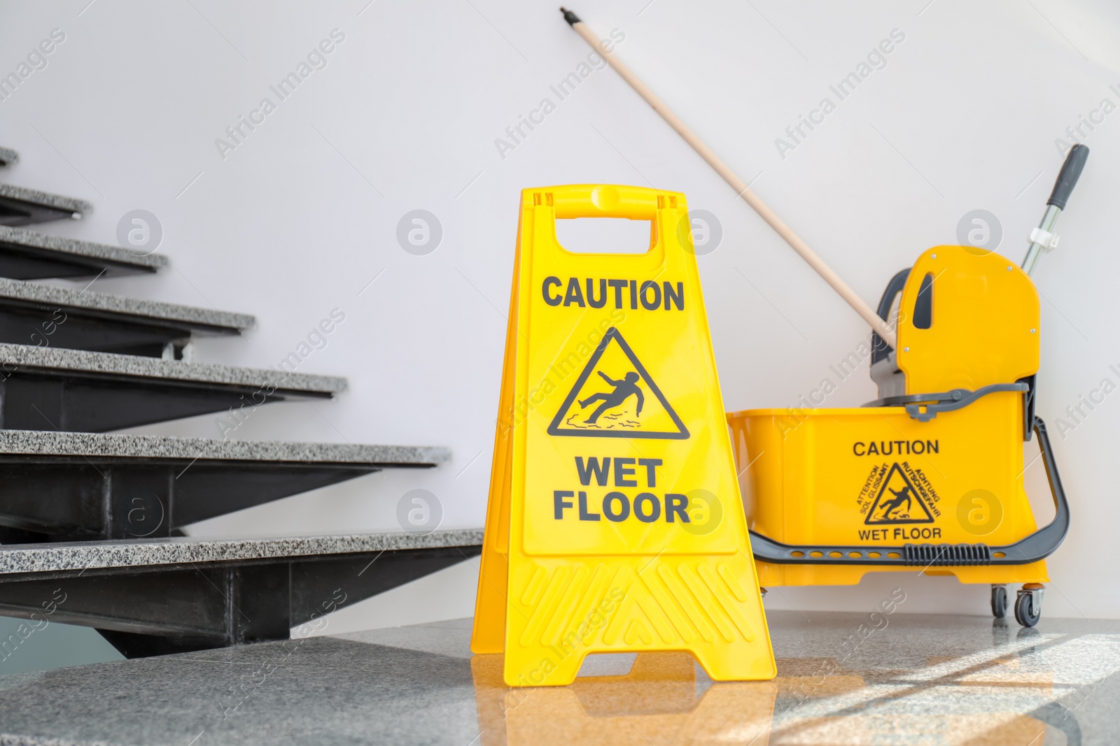 Photo of Safety sign with phrase Caution wet floor and mop bucket near stairs. Cleaning service