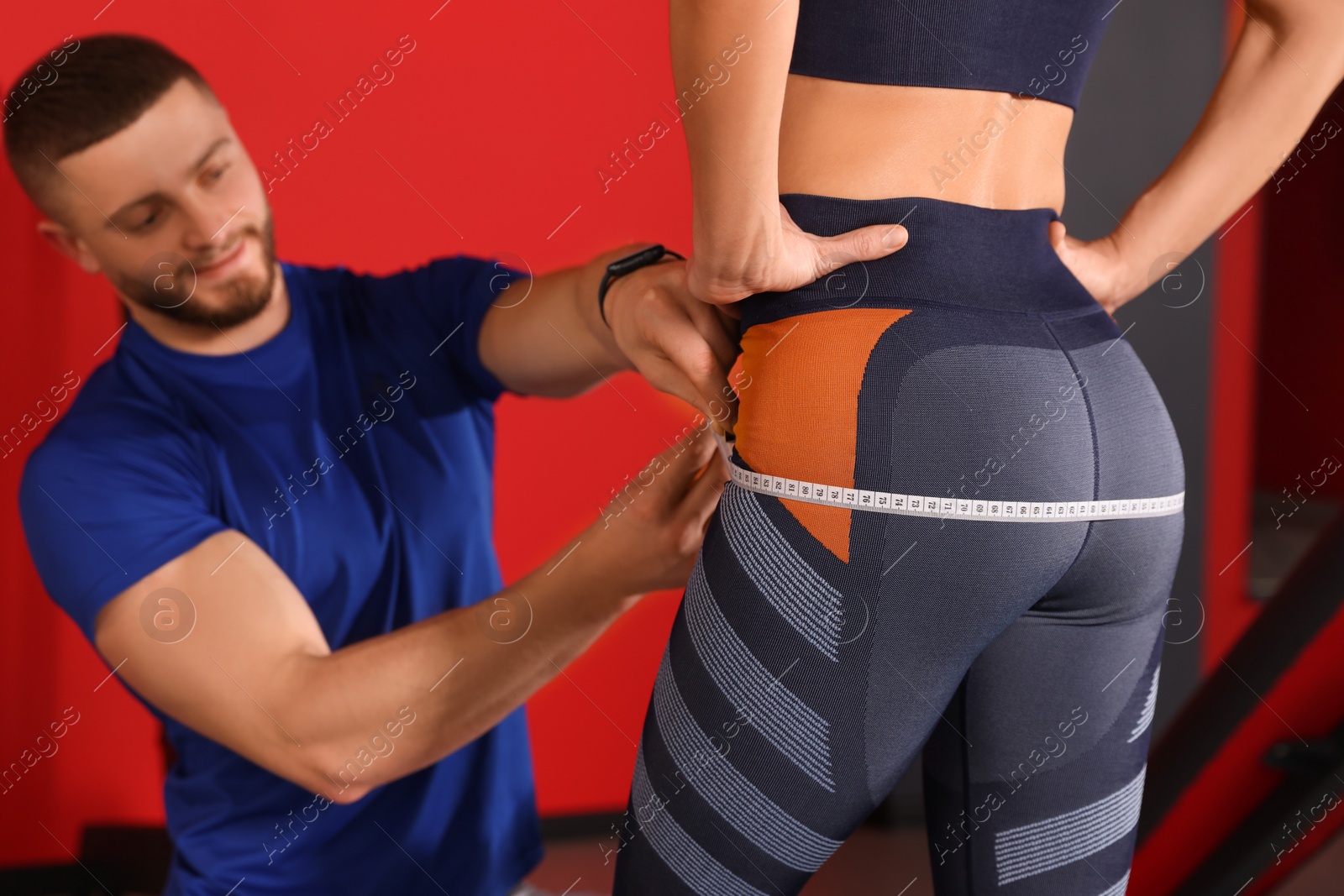 Photo of Trainer measuring woman`s hips with tape in gym, closeup