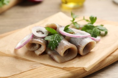 Delicious salted herring fillets with onion rings and parsley on wooden board, closeup
