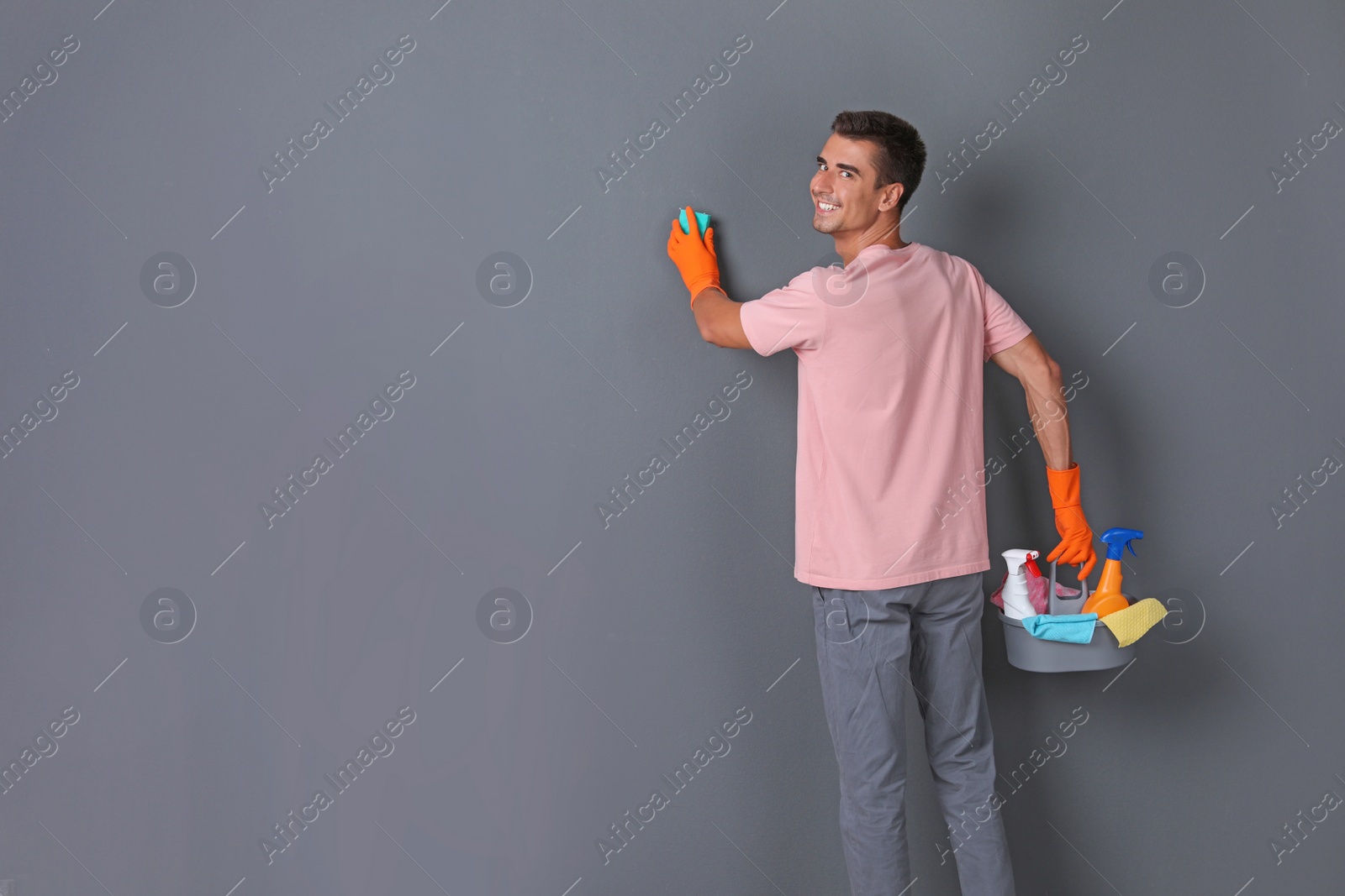 Photo of Man in gloves cleaning grey wall with sponge