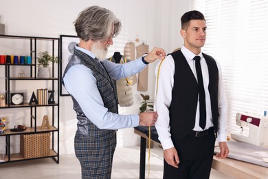 Professional tailor measuring shirt sleeve length in atelier