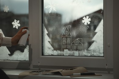 Photo of Woman using snow spray for decorating window at home, closeup