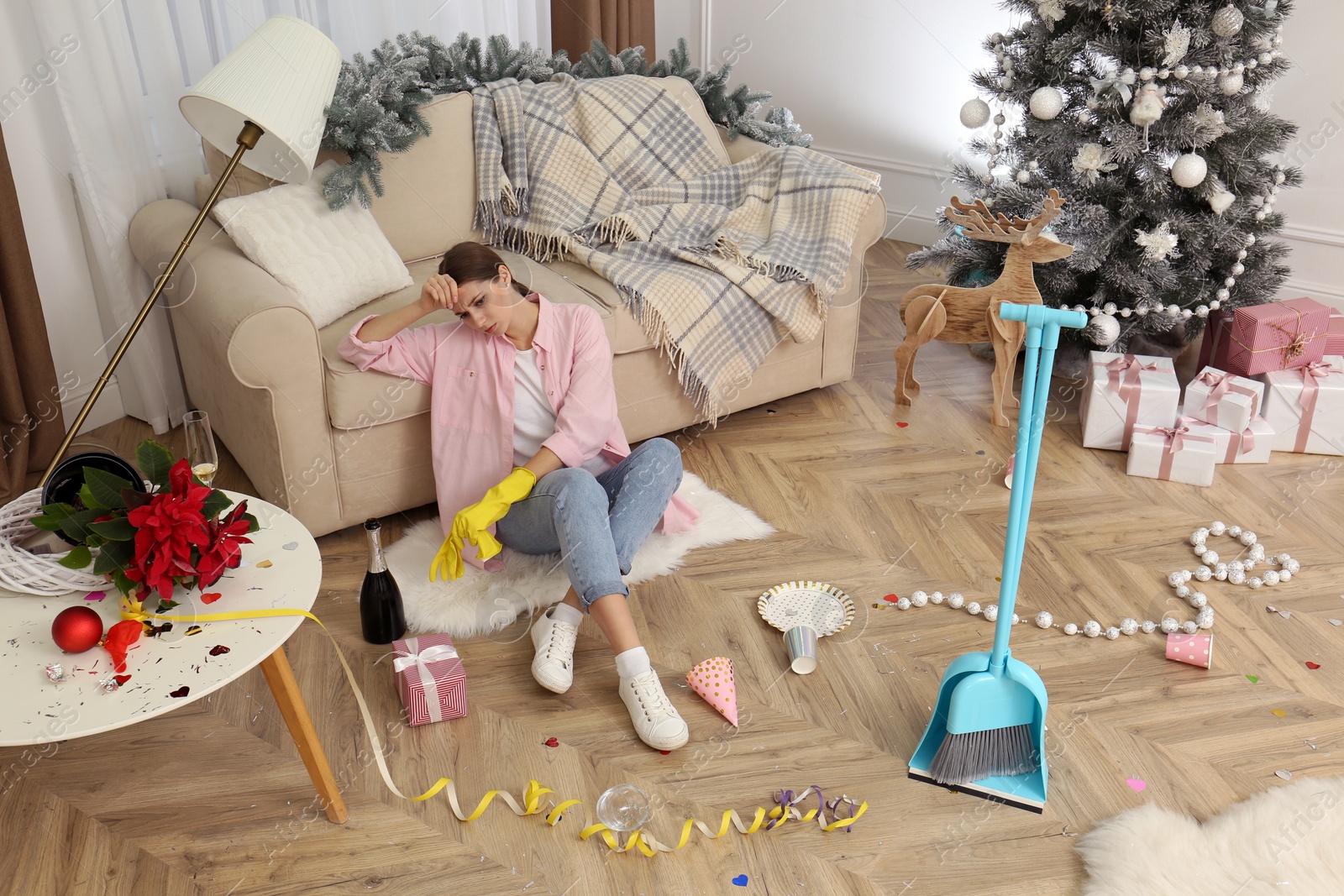 Photo of Tired woman sitting in messy room while cleaning after New Year party