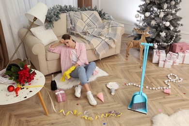 Tired woman sitting in messy room while cleaning after New Year party