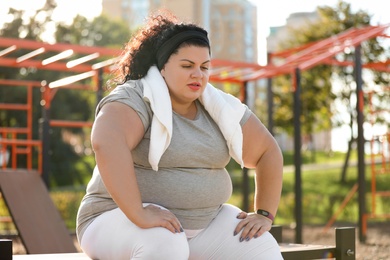 Photo of Tired overweight woman with towel resting on sports ground