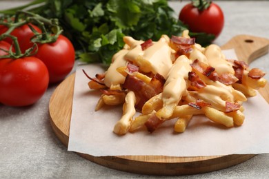 Photo of Delicious French fries with bacon, cheese sauce, tomatoes and herbs on light grey table, closeup