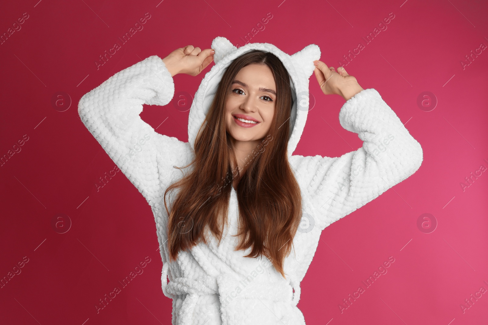 Photo of Young woman in bathrobe with funny hood on crimson background