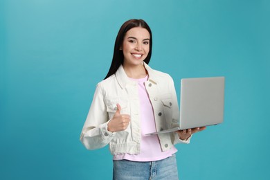 Young woman with modern laptop on light blue background