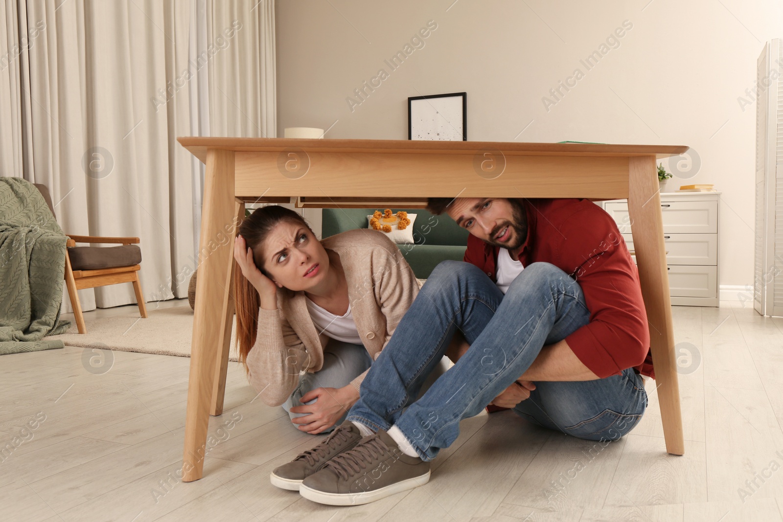 Photo of Scared couple hiding under table in living room during earthquake