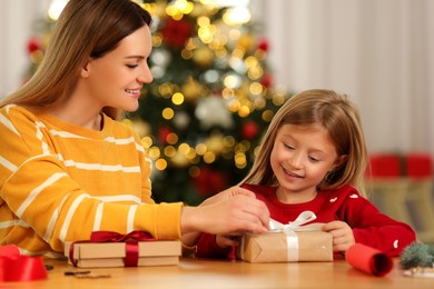 Christmas presents wrapping. Mother and her little daughter tying ribbon bows on gift boxes at home