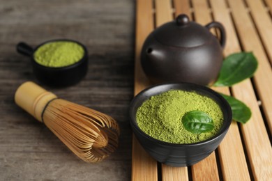 Green matcha powder, bamboo whisk and teapot on wooden table, closeup