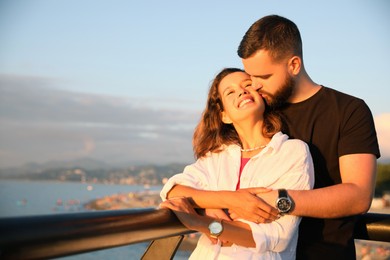 Photo of Handsome young man kissing his beautiful girlfriend on sea embankment