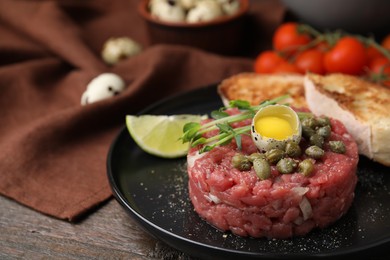 Photo of Tasty beef steak tartare served with quail egg and other accompaniments on wooden table, closeup