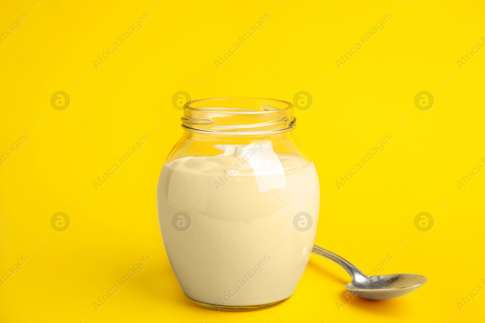 Photo of Tasty organic yogurt in glass jar on yellow background