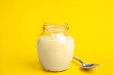 Photo of Tasty organic yogurt in glass jar on yellow background